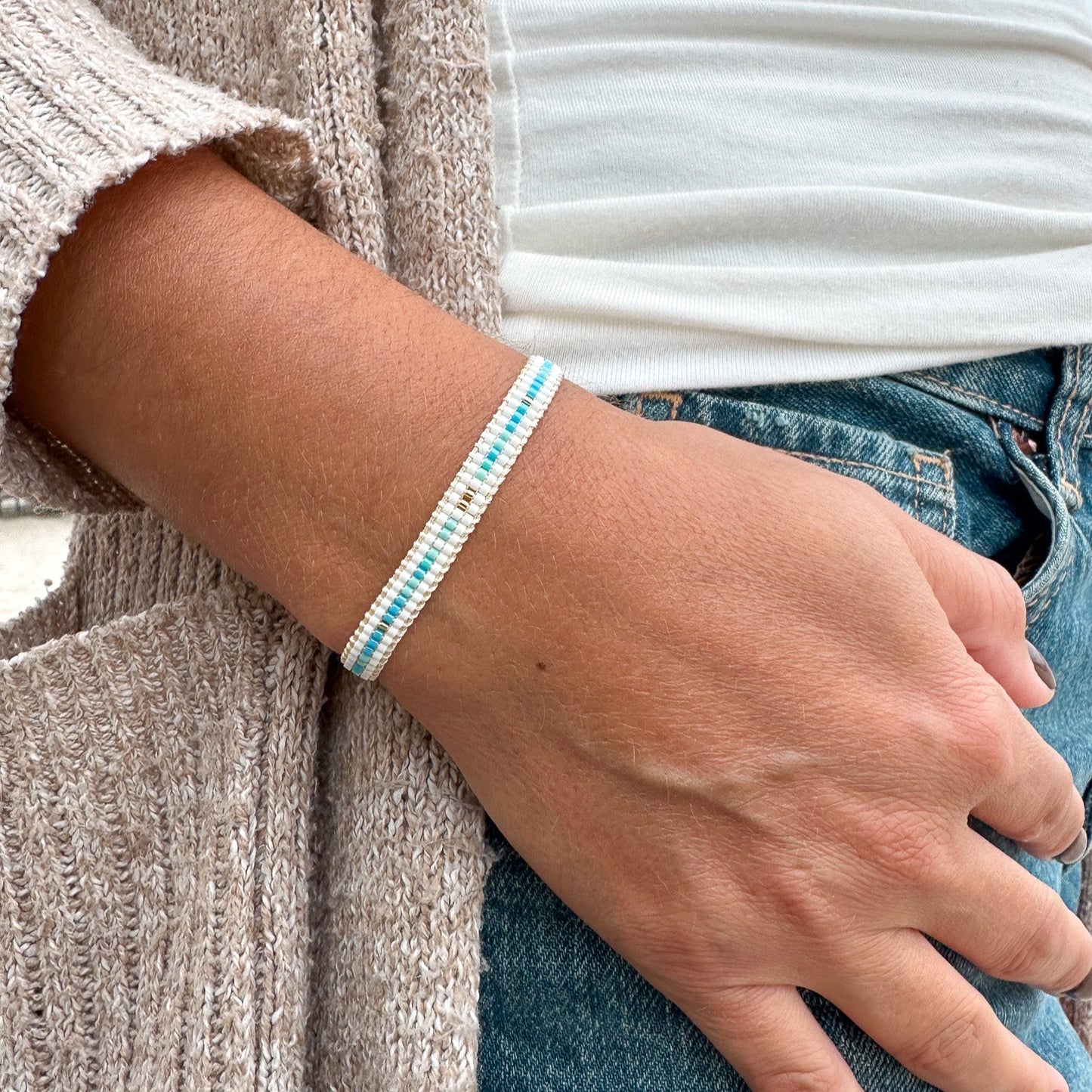 Person wearing a white and blue beaded bracelet on a neutral background