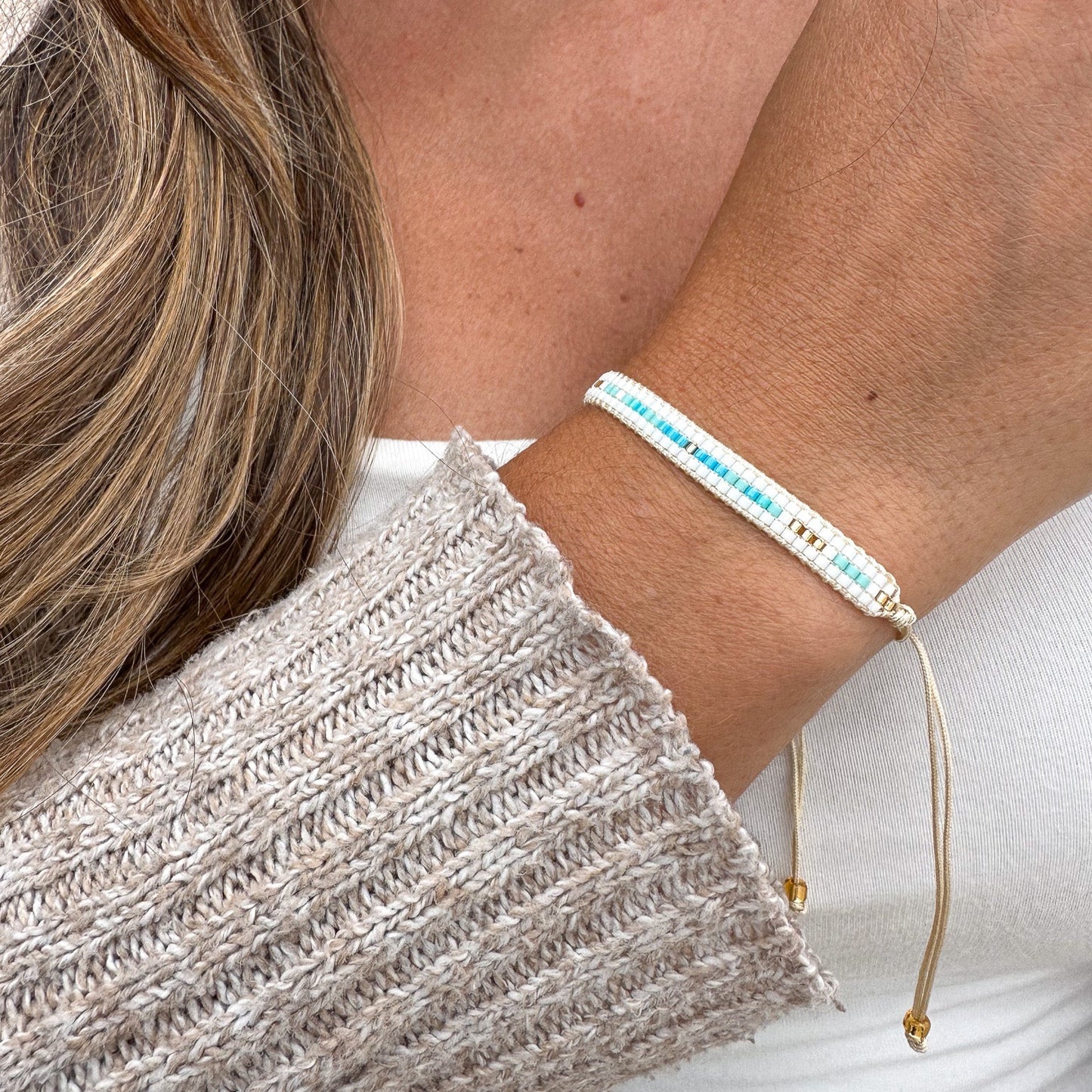 Close-up of a person wearing a bracelet with blue beads and gold accents.