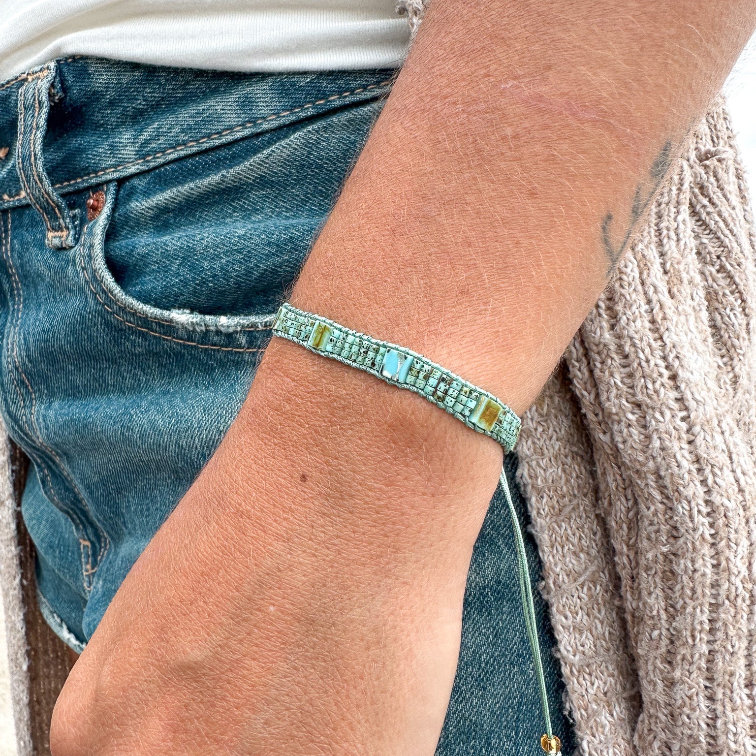 Close-up of a person wearing a blue bracelet on a casual outfit with jeans and a cardigan.
