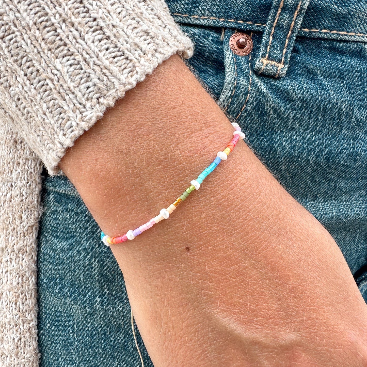 Close-up of a wrist wearing a colorful beaded bracelet with a neutral background.