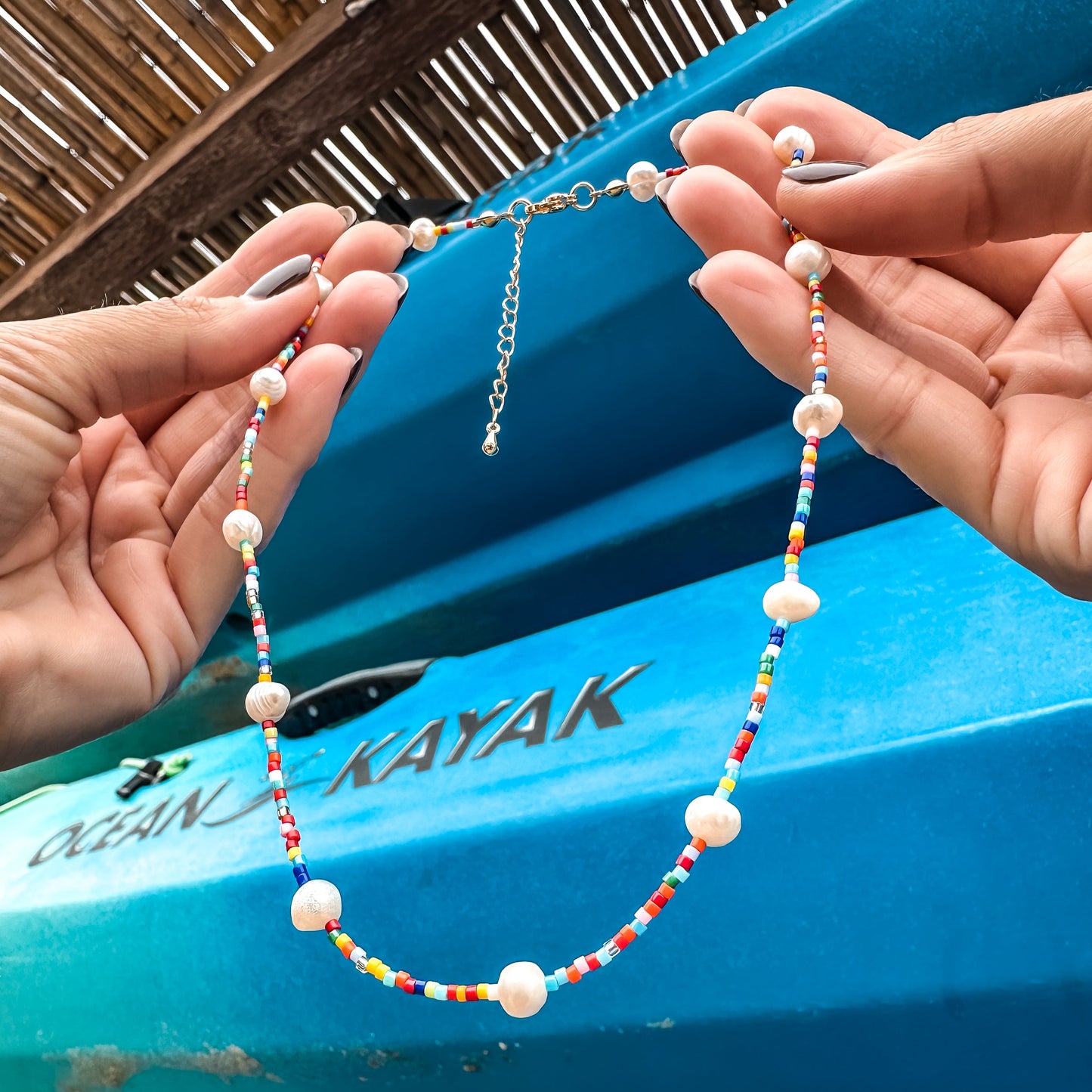 Colorful Born to Rock Jewelry beaded necklace held by hands with a blue kayak in the background