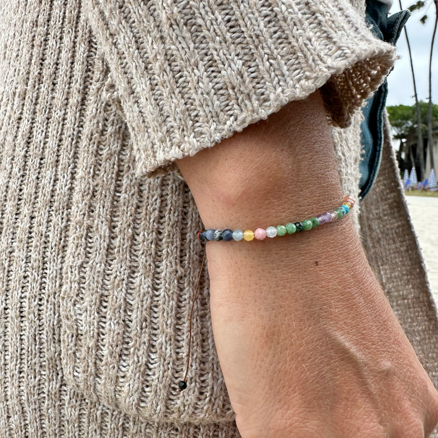 Close-up of a hand wearing a colorful beaded bracelet with a neutral sweater background.